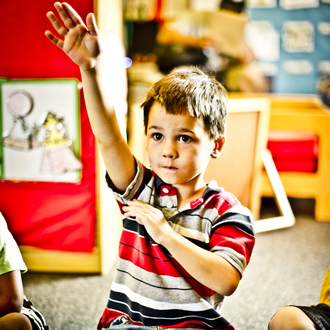 Child sitting on the floor raising his hand