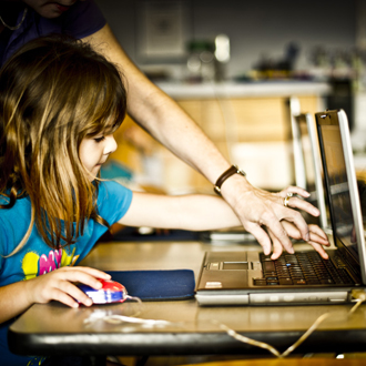 Instructor assisting child at computer workstation