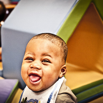 Child with smiling with bib on, sitting in play area