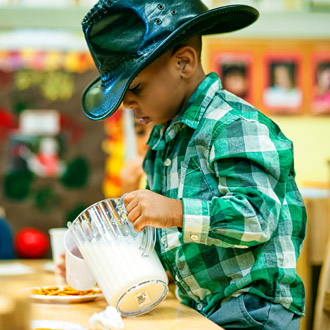 A boy wearing cowboy hat pouring milk